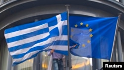 Belgium -- A man adjusts a Greek (L) and a EU flags outside the Greek embassy in Brussels, February 19, 2015